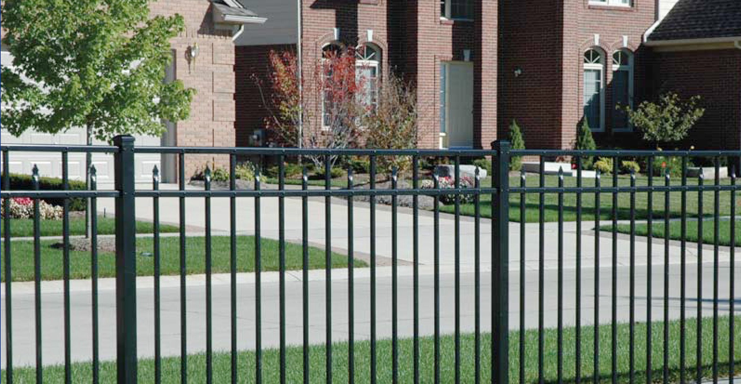 Black aluminum fence with a gate post in front of a brick home and a green lawn
