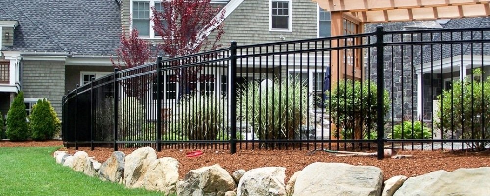 Black ornamental steel picket fence with pointed pickets in a landscaped backyard
