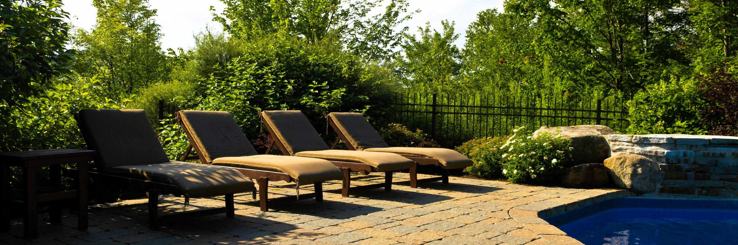 Black aluminum pool fence behind a paver pool deck with lounge chairs
