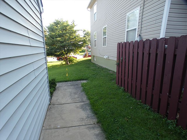 A narrow side yard in the City of St. Louis with an old reddish wood privacy fence on the right