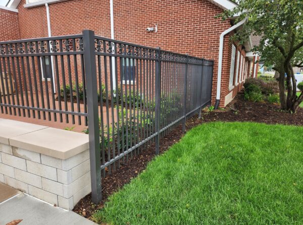 Quaker bronze commercial grade Avalanche aluminum fence with an ornamental top beside a brick building