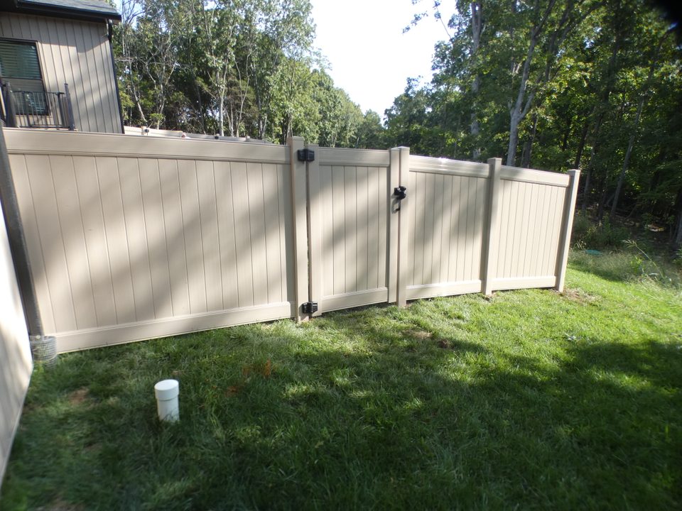 Clay colored vinyl privacy fence stepping down a slope beside a deck, with a gate in the middle and trees behind it